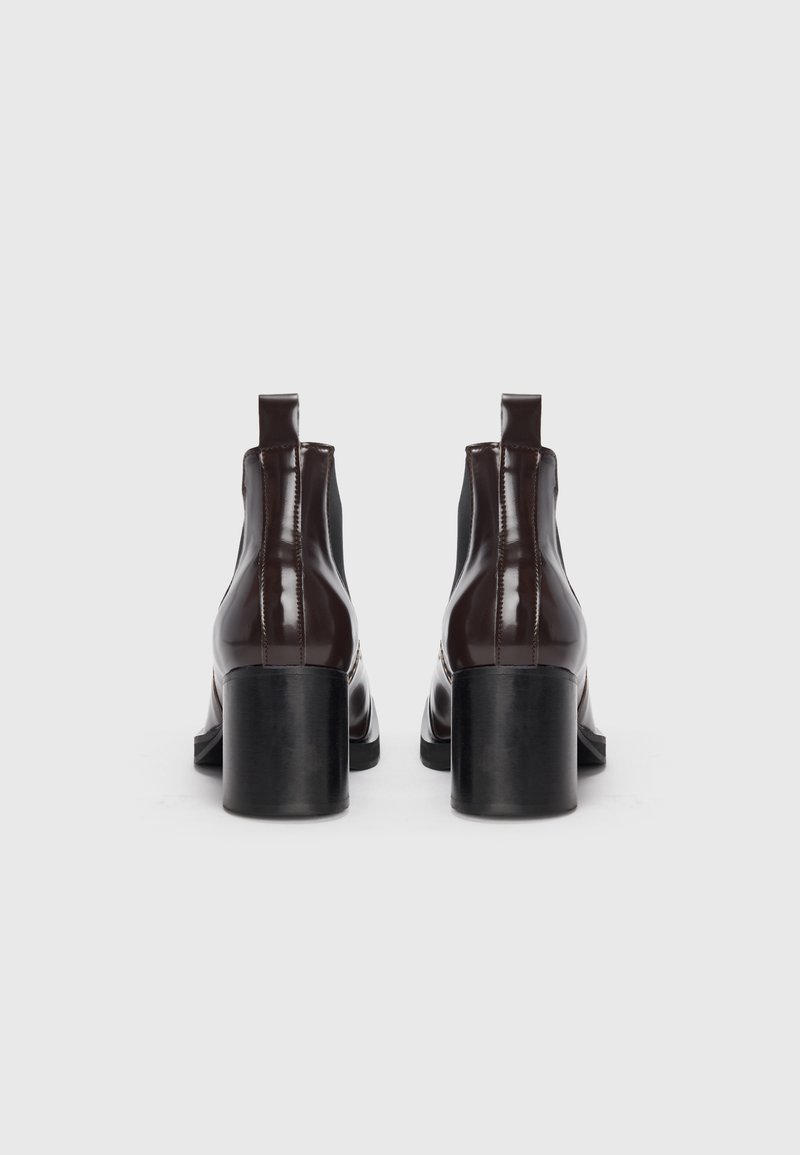 Bottines en cuir verni marron avec un large talon noir, des panneaux élastiques sur les côtés et des languettes à l'arrière pour un enfilage facile.