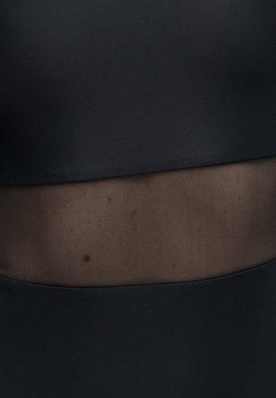 Tissu noir avec un panneau en maille transparente au centre laissant apparaître la peau et un petit grain de beauté foncé sur la peau exposée.