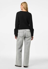 Suéter negro de punto con mangas anchas y lazos, combinado con vaqueros de pierna ancha de un gris claro. La tela es suave y tiene una textura sutil.