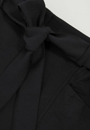 Top in tessuto nero con dettaglio a fiocco in vita, texture liscia e design strutturato con pieghe e cuciture sottili.