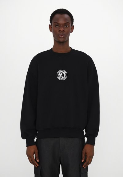 Sweatshirt noir avec des poignets et un ourlet côtelés, présentant un logo circulaire blanc sur la poitrine. Fabriqué en tissu doux avec une coupe décontractée.
