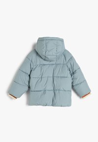 Chaqueta de plumas azul claro con capucha, diseño acolchado, puños elásticos y un suave forro interior. Presenta un corte relajado y de gran tamaño.