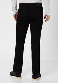 Black denim jeans with straight cut, featuring back pockets and minimal stitching details. Worn with black footwear and light gray top.