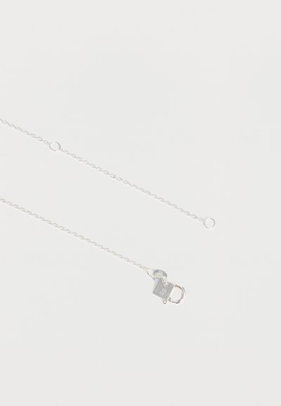 Collier délicat en chaîne d'argent avec un petit fermoir mousqueton et un maillon ovale réglable près du fermoir sur un fond blanc uni.
