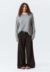 Pull en tricot gris au fit décontracté, associé à un pantalon noir taille haute à larges jambes. Les sandales présentent des fines lanières. Design minimaliste.