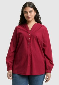 Karmesinrote Bluse mit langen Ärmeln, strukturiertem Stoff, drei Knöpfen am Ausschnitt und einer linken Brusttasche. Standardpassform mit abgerundetem Saum.