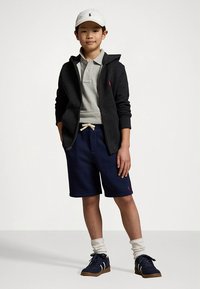 Pilkas bliuzonas su užtrauktuku dėvimas ant pilkos polo marškinėlių, prie jo derinamos tamsiai mėlynos šortai ir baltos kojinės. Balta kepuraitė ir tamsūs sportbačiai užbaigia aprangą.