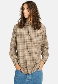 Beige karierte Hemdbluse mit langen Ärmeln, versehen mit einem kragen und dezenter Textur, kombiniert mit hellblauen Jeans.