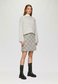 Szary, oversize sweter, mini spódnica w kraciasty wzór oraz czarne botki za kostkę z grubą podeszwą. Miękka tekstura, luźny krój i warstwowy wygląd.