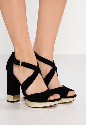Black suede high-heeled sandals with crossed ankle straps, open toe, and gold-textured block heel accents.