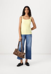 Yellow ribbed tank top, blue wide-leg jeans, and a brown handbag. The top features a square neckline with thin straps. Shoes are black loafers.