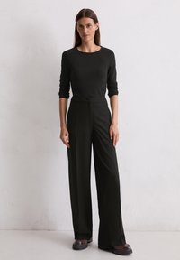Zwarte lange mouw top met een ronde halslijn, gecombineerd met hoge zwarte wijde broek. Glad materiaal, nauwsluitende pasvorm, minimalistisch ontwerp.