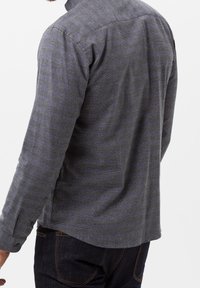 Koszula z długim rękawem w ciemnoszarym kolorze z subtelnym wzorem w kratę. Posiada kołnierzyk zapinany na guziki oraz zaokrąglony dół. Materiał wydaje się być teksturowany.