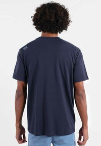 T-shirt en coton bleu marine à manches courtes, coupe décontractée, avec une petite étiquette sur l'épaule gauche ; texture lisse, design simple.