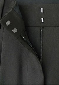 Zwarte op maat gemaakte broeken van een gladde stof, met een zijrits, metalen drukknoopsluitingen en een gestructureerde tailleband met contrasterende accenten.