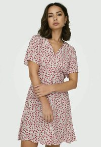 Floral short dress with a V-neck, short sleeves, and a fitted waist. Light fabric with red roses on a cream background. Scalloped hem.