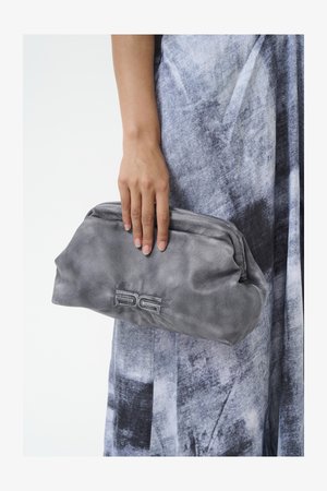 Clutch en cuir gris avec une surface douce et texturée et une fermeture éclair. Présente un logo embossé à l'avant. Se tient d'une main.