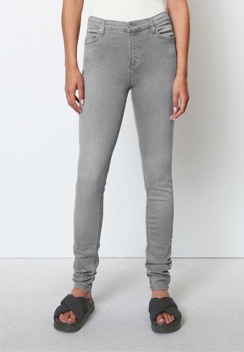 Jeans ajustados de mezclilla gris con cintura de medio tiro, bolsillos frontales y un ajuste ceñido. Presentan una textura suave y un lavado sutil. Calzado casual.