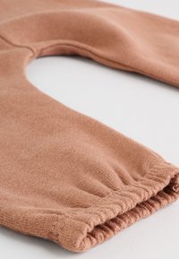 Roostevärvi kangast retuusid kogutud elastsete mansettidega, pehme tekstuur ja sile viimistlus, rõhutades lihtsat ja funktsionaalset disaini.