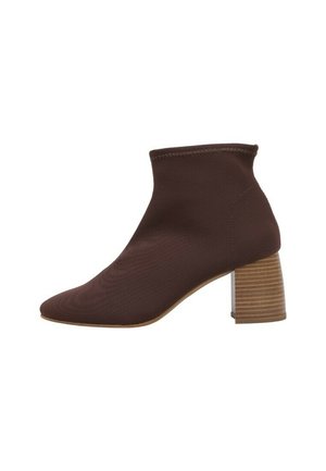 Bota corta marrón con parte superior de tela texturizada y tacón de bloque apilado, mostrada desde el lado exterior sobre un fondo blanco.