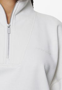 Pullover bianco a mezza zip realizzato in tessuto testurizzato, con zip argento e logo in rilievo sul lato destro.