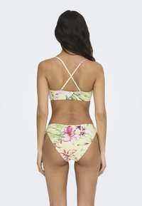 Ensemble de bikini avec une base jaune ornée de grands motifs floraux roses et verts. Bretelles croisées ajustables à l'arrière. Texture de tissu lisse.