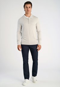 Polo a maniche lunghe grigio chiaro con colletto con zip, abbinato a chinos blu scuro e sneakers bianche, esposto su uno sfondo semplice.