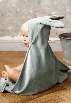 Asciugamano con cappuccio a tema coniglietto in cotone grigio, con orecchie sovradimensionate, che pende su un bambino seduto su un pavimento di legno, mostrando una texture morbida e un design informale.