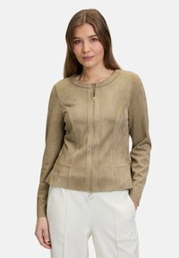 Beige suède jack met een ronde halslijn, ritssluiting aan de voorkant en twee zijzakken; aansluitend ontwerp met naaddetails langs de torso.
