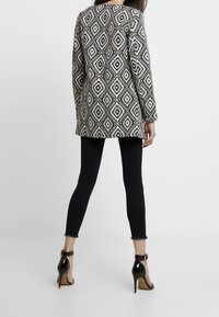 Cappotto lungo a righe bianche e nere con un motivo a rombi, abbinato a jeans skinny neri e scarpe con tacco alto nere.