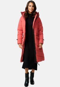 Garšs, pūkains korallkrāsas mētelis ar kapuci, ar šuvēm paneļiem un divām priekšējām kabatām, apvienots ar melnu ribotu kleitu un melniem potīšu zābakiem.