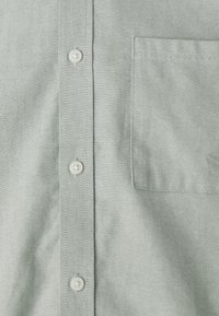 Lichtgroene button-up shirt van textuurstof, met een borstzak en witte knopen aan de voorkant.
