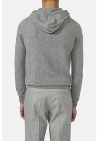 Grau Hoodie aus weichem Stoff, mit lockerer Passform und großzügiger Kapuze. Kombiniert mit maßgeschneiderten grauen Hosen, die eine feine Textur und klare Linien zeigen.