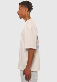 Utility t-shirt i creme bomuld med korte ærmer, en afslappet pasform og et abstrakt blåt og pink grafisk design på ryggen.