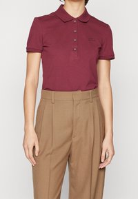Polo en bordeaux avec un col classique et trois boutons, associé à un pantalon taille haute, ajusté, de couleur marron clair.