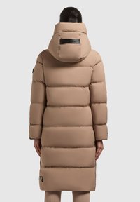 Manteau doudoune beige avec une capuche, présentant des sections matelassées horizontales, un patch logo au dos et un ourlet légèrement évasé.