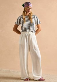 Raipe puuvillane T-särk tumesinises ja valges, koos vabade valgete pükste ja elastse vöökohtaga ning roosade liugjalatsitega.