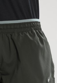 Tummanvihreät urheilushortsit, joissa on joustava vyötärö ja vaaleansininen accentti. Sisältää pienen valkoisen Nike-logon alareunassa.
