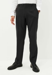 Musta räätälöity housut, jotka on valmistettu sileästä kankaasta, varustettu napilla, sivutaskuilla ja suoralla lahkeella, yhdistettynä mustiin kenkiin.