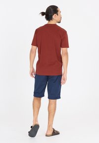 Kortärmad vinröd t-shirt i kombination med knälånga marinblå shorts, med uppvikt ärm och bruna sandaler med texturerad sula.