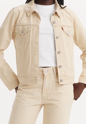 Person iført beige og hvide vertikale stribede denimjakke og bukser med en ensfarvet hvid cropped top.