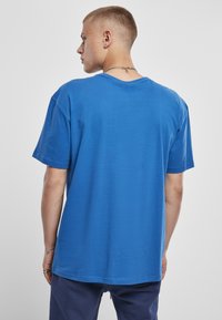 Tricou din bumbac albastru cu o croială lejeră, mâneci scurte și o textură netedă. Prezintă un decolteu rotund și un design simplu.