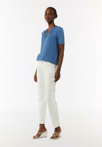 Niebieski krótki top z dekoltem w serek, w zestawieniu z białymi slim-fit spodniami i białymi sandałami na koturnie. Gładki materiał o minimalistycznym wzornictwie.