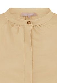 Blouse beige avec un col rond, fermeture par boutons à l'avant, tissu doux, détails plissés sous le col et une étiquette de marque au niveau du cou.