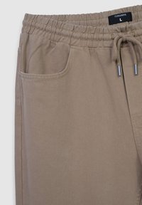 Joggery w kolorze taupe wykonane z dzianiny bawełnianej. Posiadają elastyczny pas z regulowanym sznurkiem, boczną kieszeń oraz teksturowany diagonalny wzór.