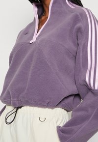 Fleece-pullover i ljuslila med hög krage, kontrasterande dragkedja i ljusrosa och sidostrecken. Har elastisk nederkant och dragsko.