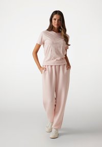 Light pink T-shirt with subtle pattern, paired with loose-fitting, light pink sweatpants and white sneakers, featuring pockets.