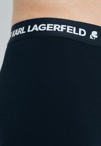 Boxer shorts noirs avec une texture lisse, comportant une ceinture étiquetée "KARL LAGERFELD" en blanc. Design simple, coupe ajustée.