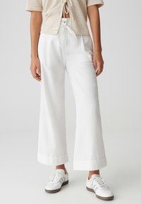 White wide-leg trousers made of lightweight fabric, featuring a high waist, pleats, and rolled hems. Paired with white sneakers.