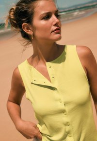 Débardeur jaune à côtes sans manches avec un devant à boutons et un col légèrement asymétrique. Texture lisse avec des détails simples.